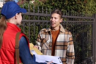 Photo of Young man receiving envelope from postwoman outdoors