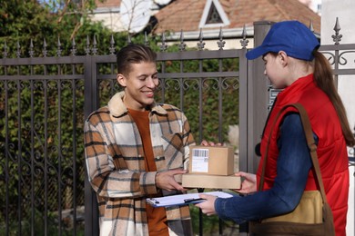 Photo of Postwoman giving parcels to young man outdoors