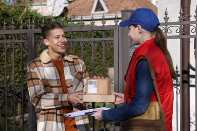 Photo of Postwoman giving parcels to young man outdoors