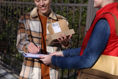 Photo of Man signing papers while receiving parcel from postwoman outdoors, closeup