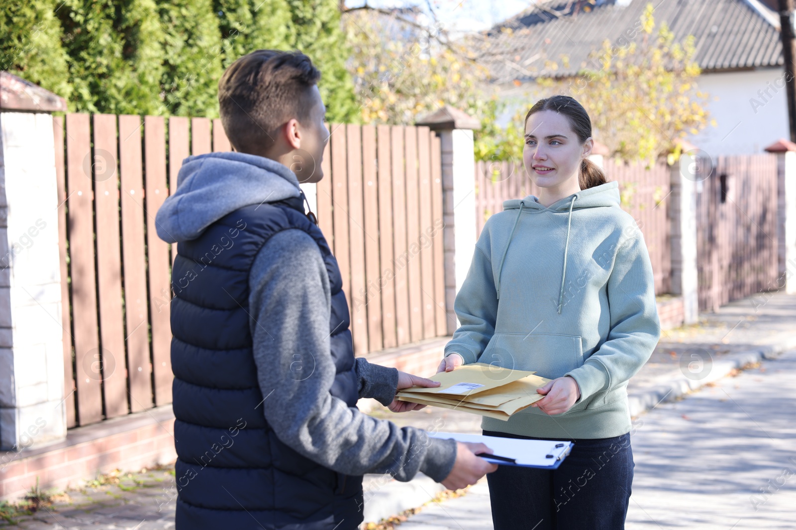 Photo of Postman with clipboard giving envelopes to woman outdoors