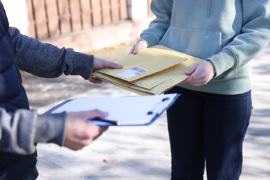 Photo of Postman giving envelopes to woman outdoors, closeup