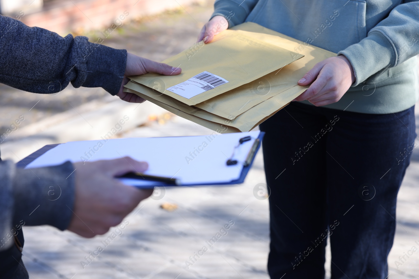 Photo of Postman giving envelopes to woman outdoors, closeup