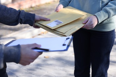 Photo of Postman giving envelopes to woman outdoors, closeup