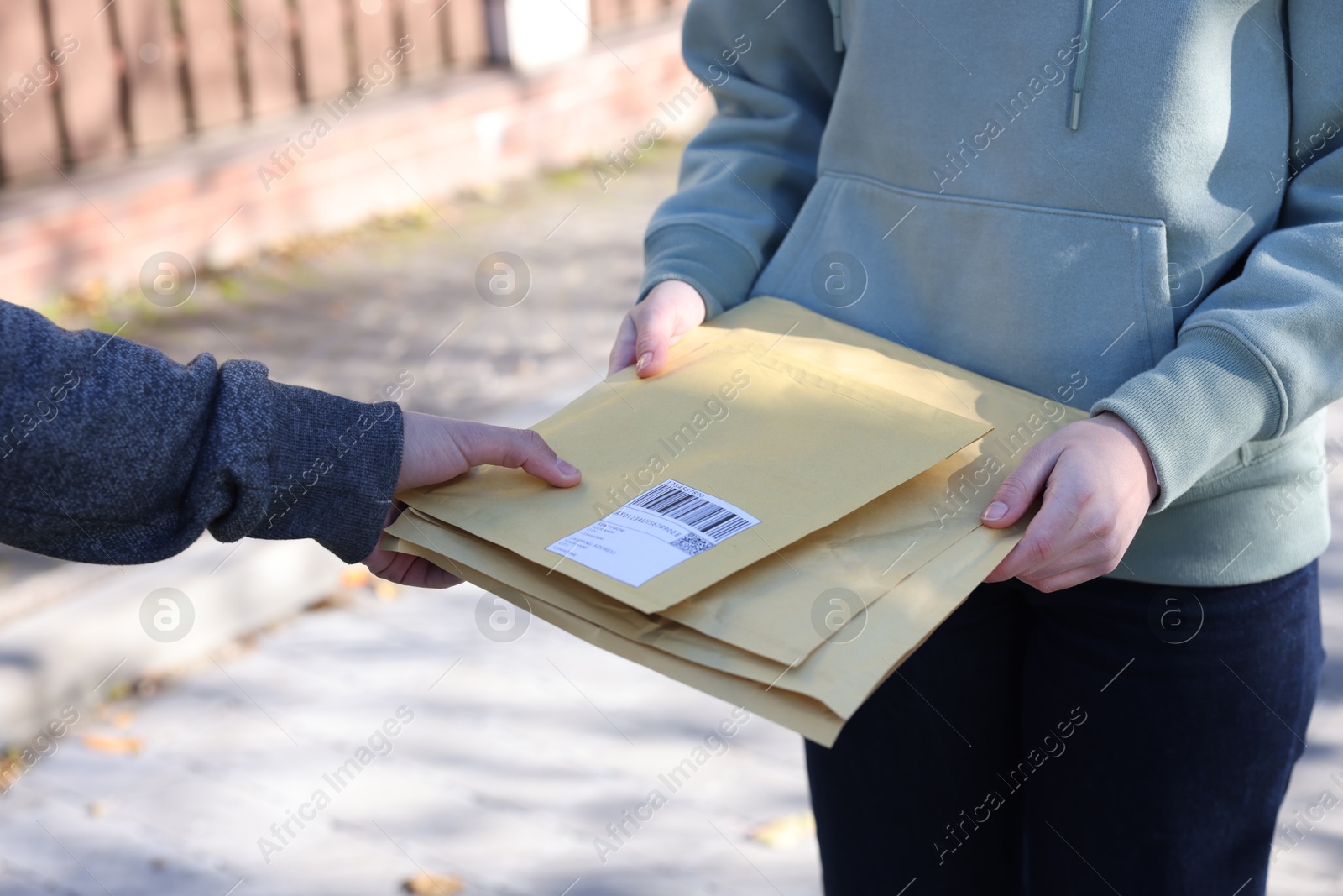 Photo of Postman giving envelopes to woman outdoors, closeup