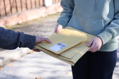 Photo of Postman giving envelopes to woman outdoors, closeup