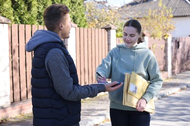 Photo of Woman signing papers while receiving parcel from postman outdoors