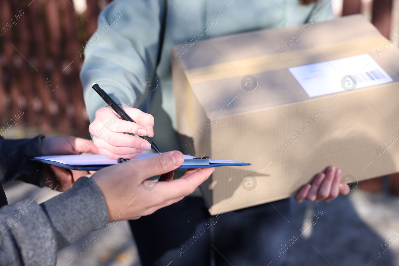 Photo of Woman signing papers while receiving parcel from postman outdoors, closeup