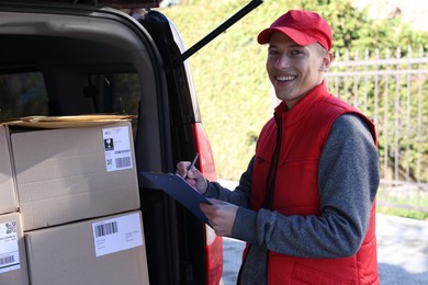 Postman with clipboard near car full of parcels outdoors