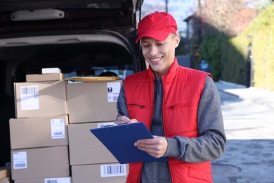 Photo of Postman with clipboard near car full of parcels outdoors