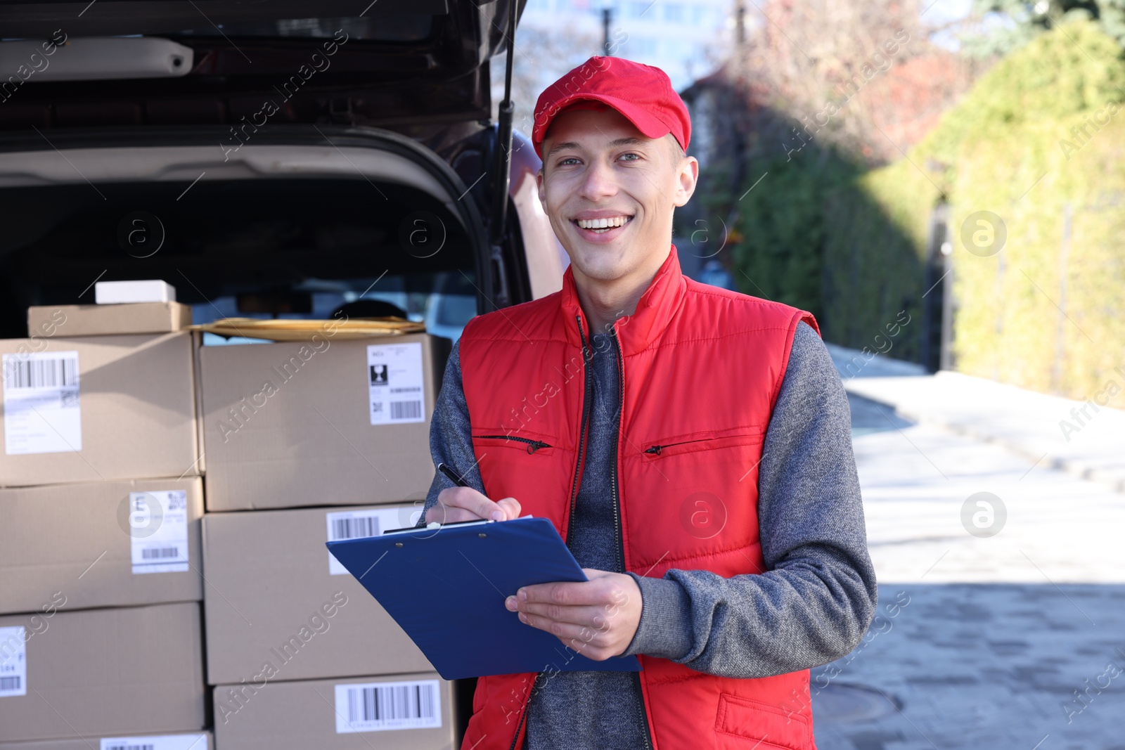 Photo of Postman with clipboard near car full of parcels outdoors