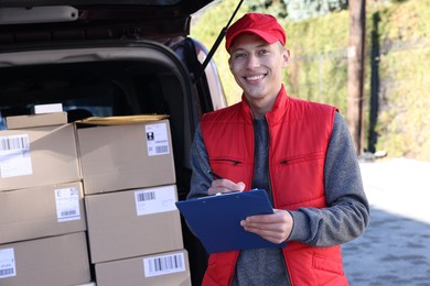 Photo of Postman with clipboard near car full of parcels outdoors