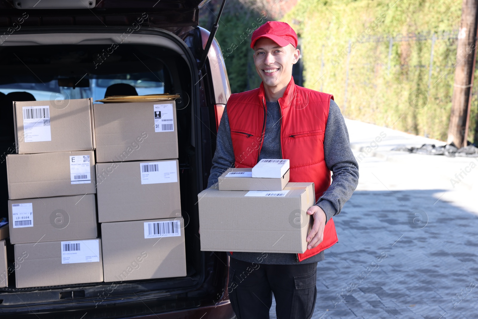 Photo of Happy postman with parcels near car outdoors