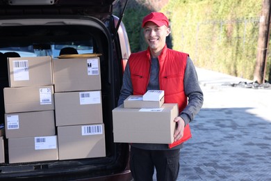 Happy postman with parcels near car outdoors