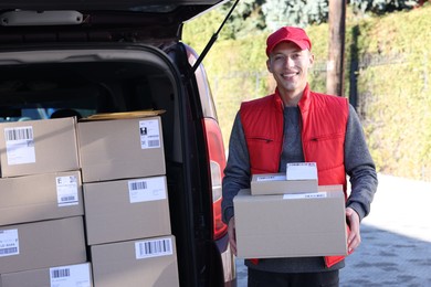 Happy postman with parcels near car outdoors