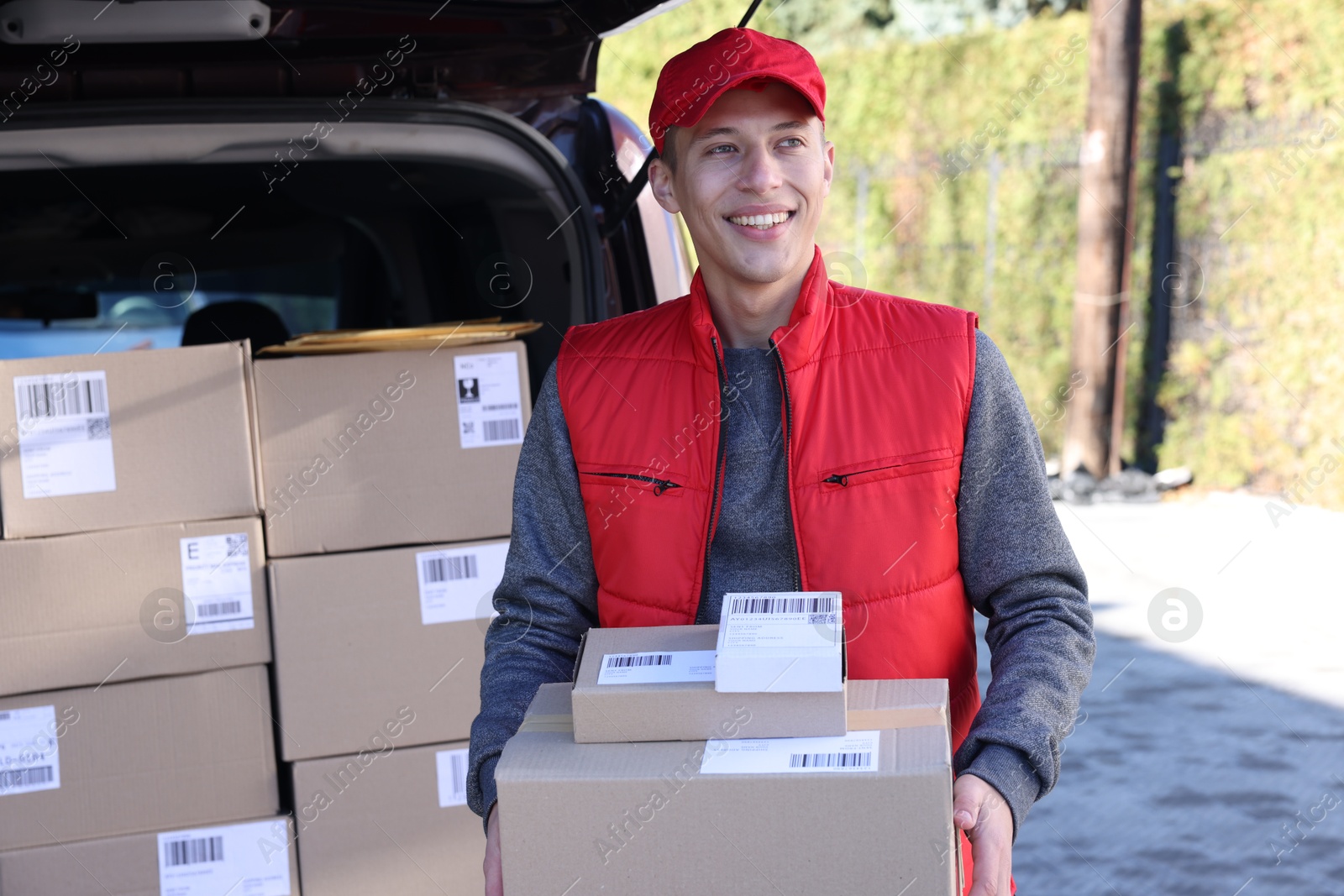 Photo of Happy postman with parcels near car outdoors