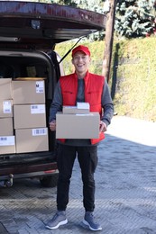 Happy postman with parcels near car outdoors