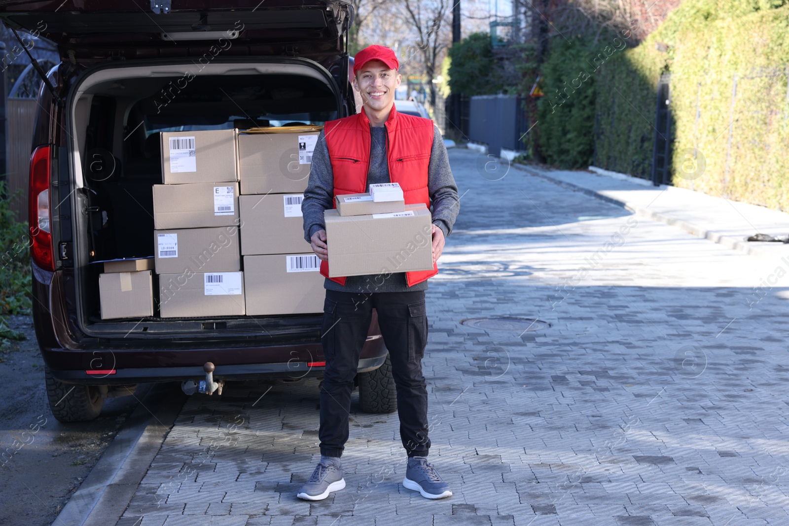 Photo of Happy postman with parcels near car outdoors