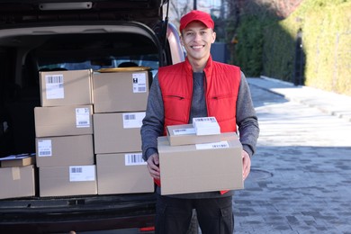 Happy postman with parcels near car outdoors