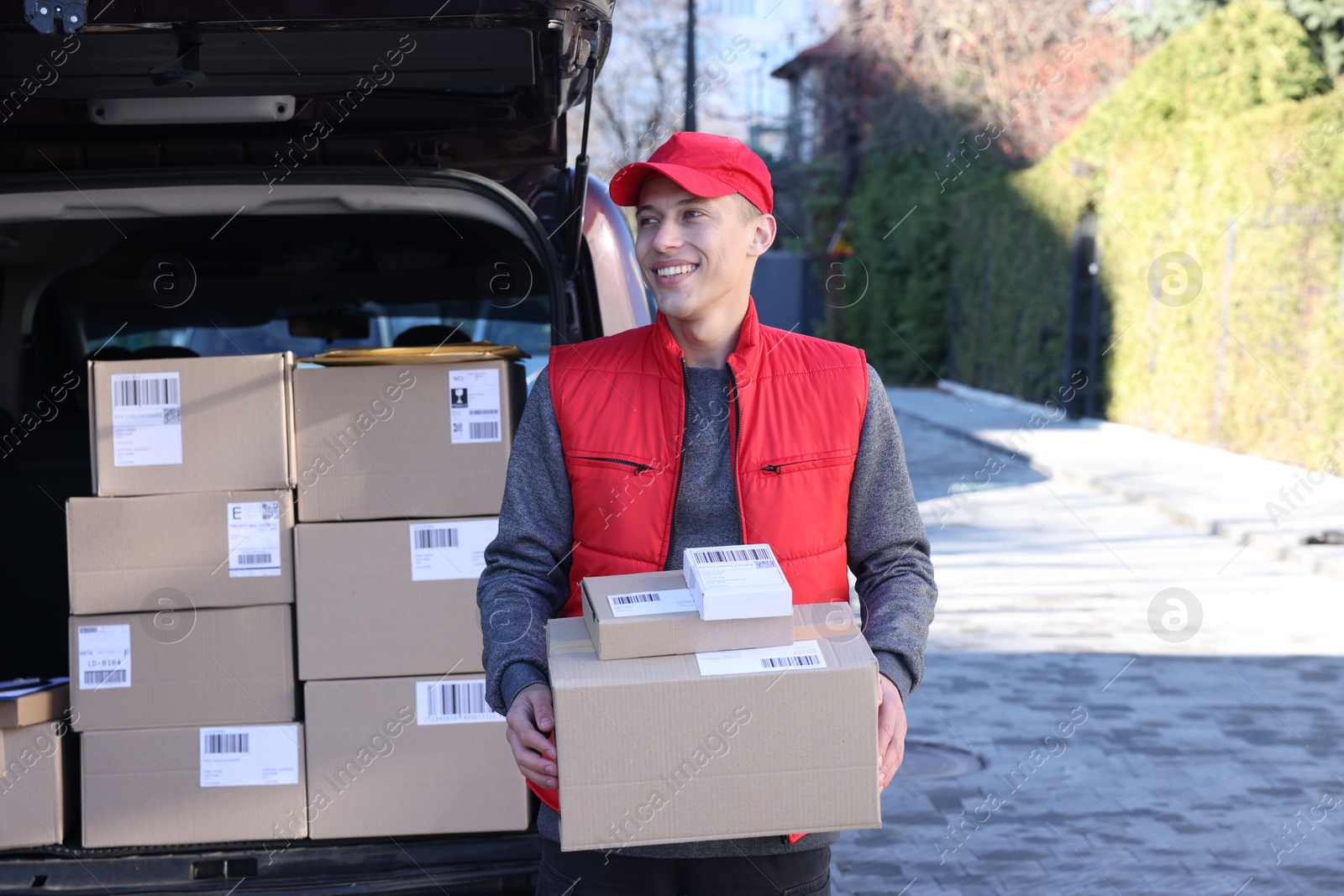 Photo of Happy postman with parcels near car outdoors