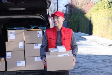 Photo of Happy postman with parcels near car outdoors