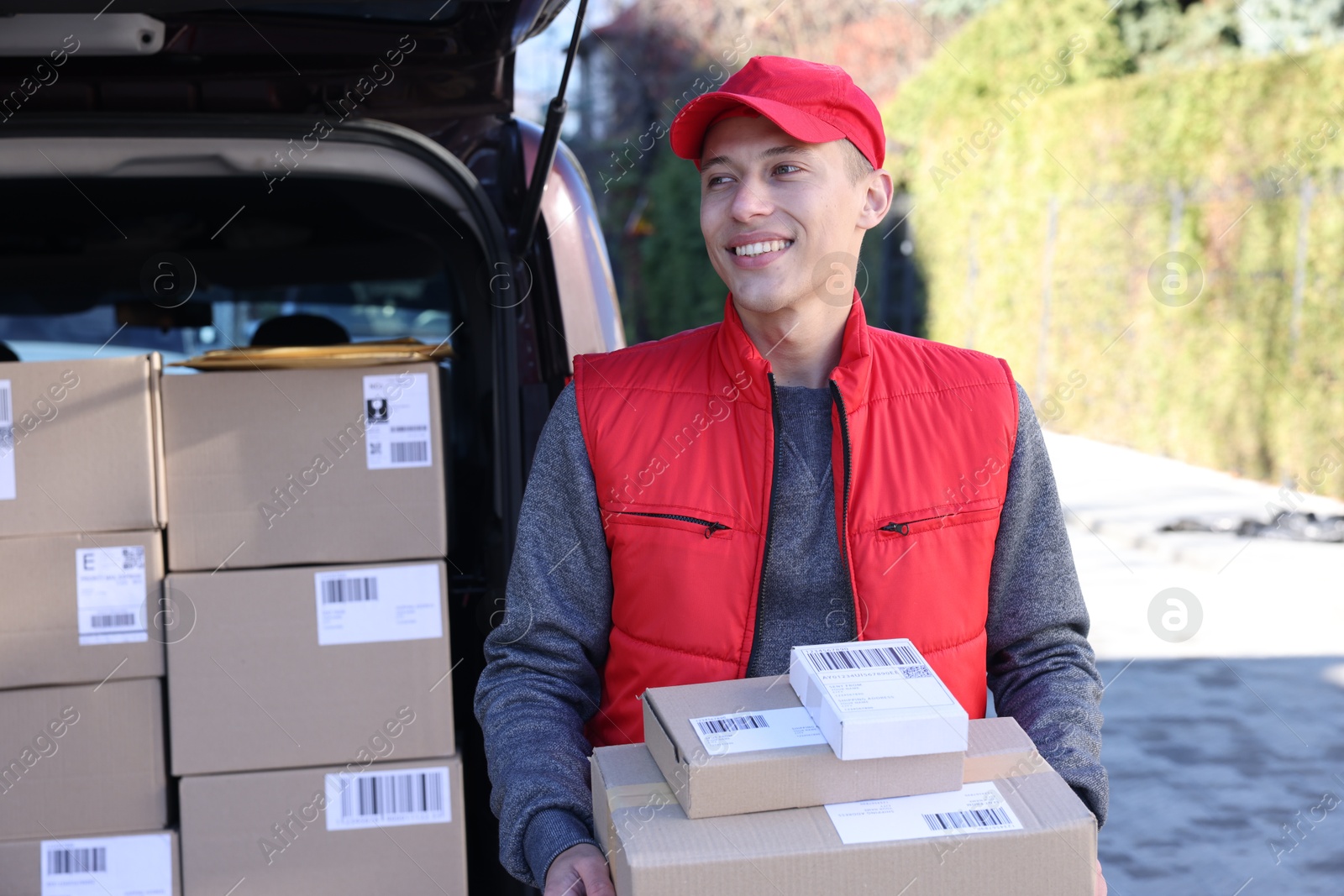 Photo of Happy postman with parcels near car outdoors