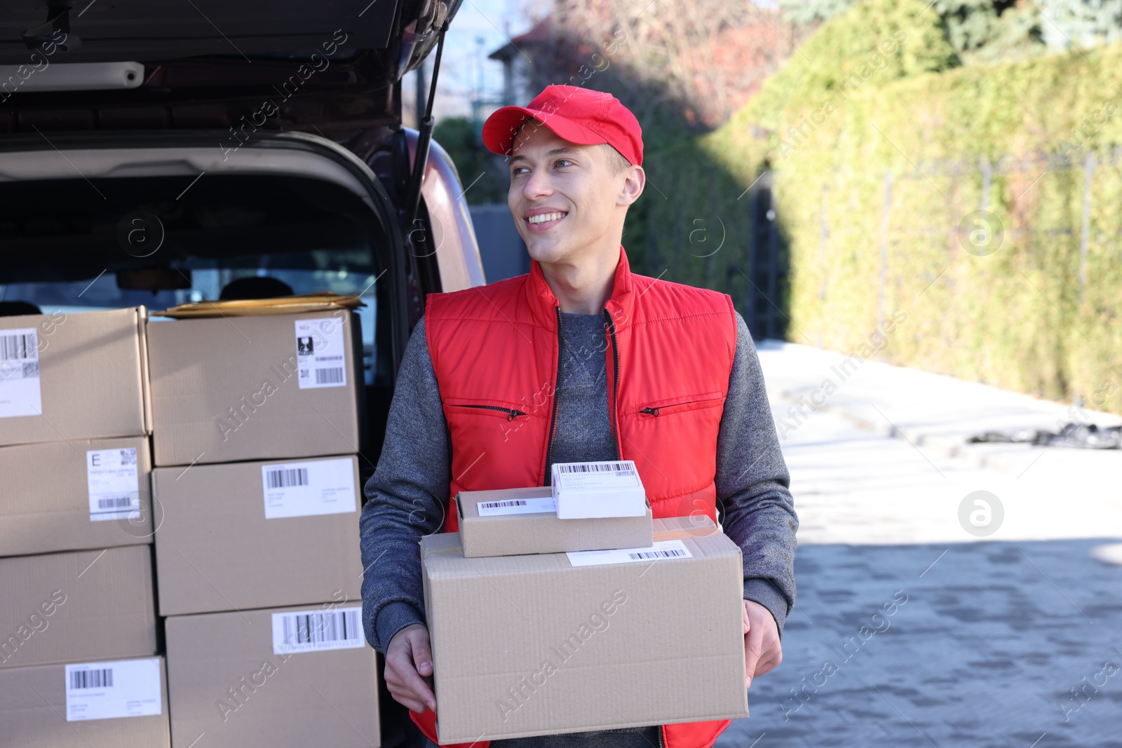 Photo of Happy postman with parcels near car outdoors