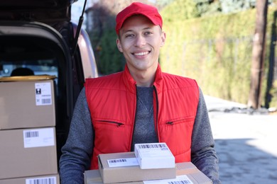 Happy postman with parcels near car outdoors