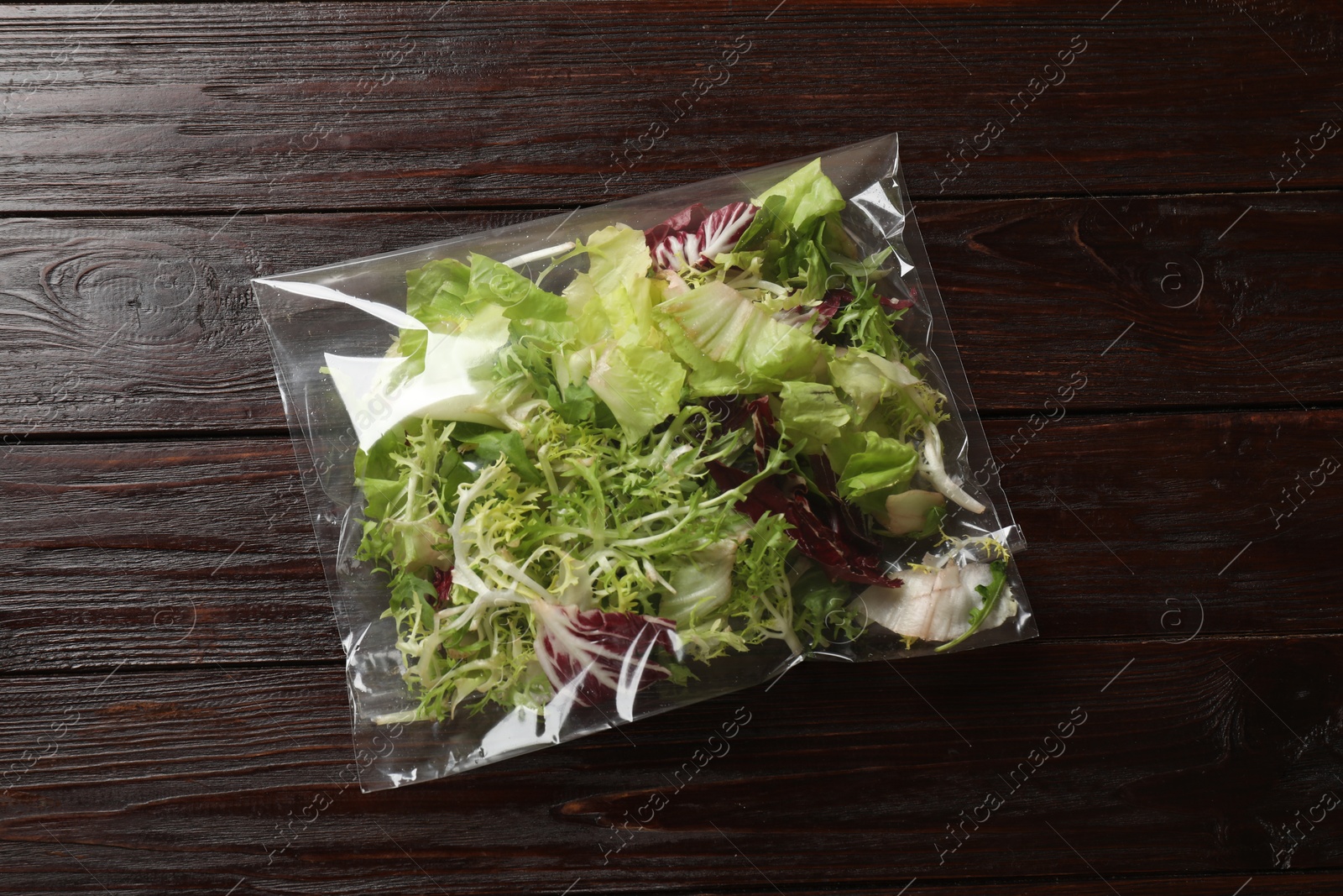 Photo of Pack of fresh salad mix on wooden table, top view