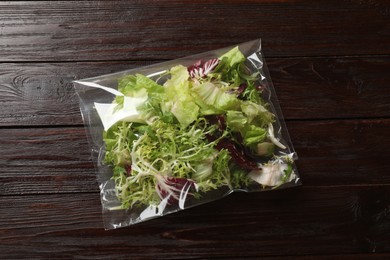 Photo of Pack of fresh salad mix on wooden table, top view