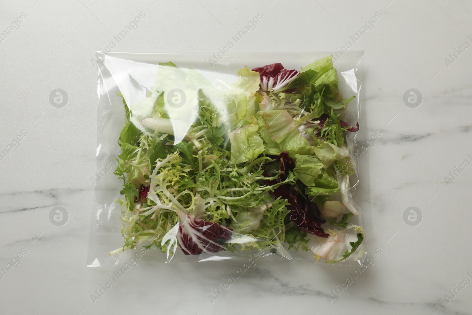 Photo of Pack of fresh salad mix on white marble table, top view