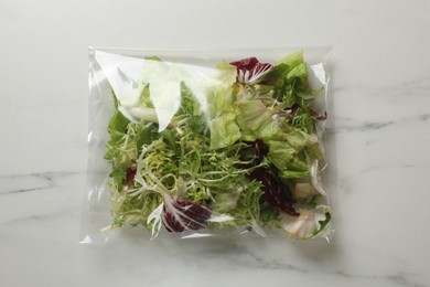 Photo of Pack of fresh salad mix on white marble table, top view