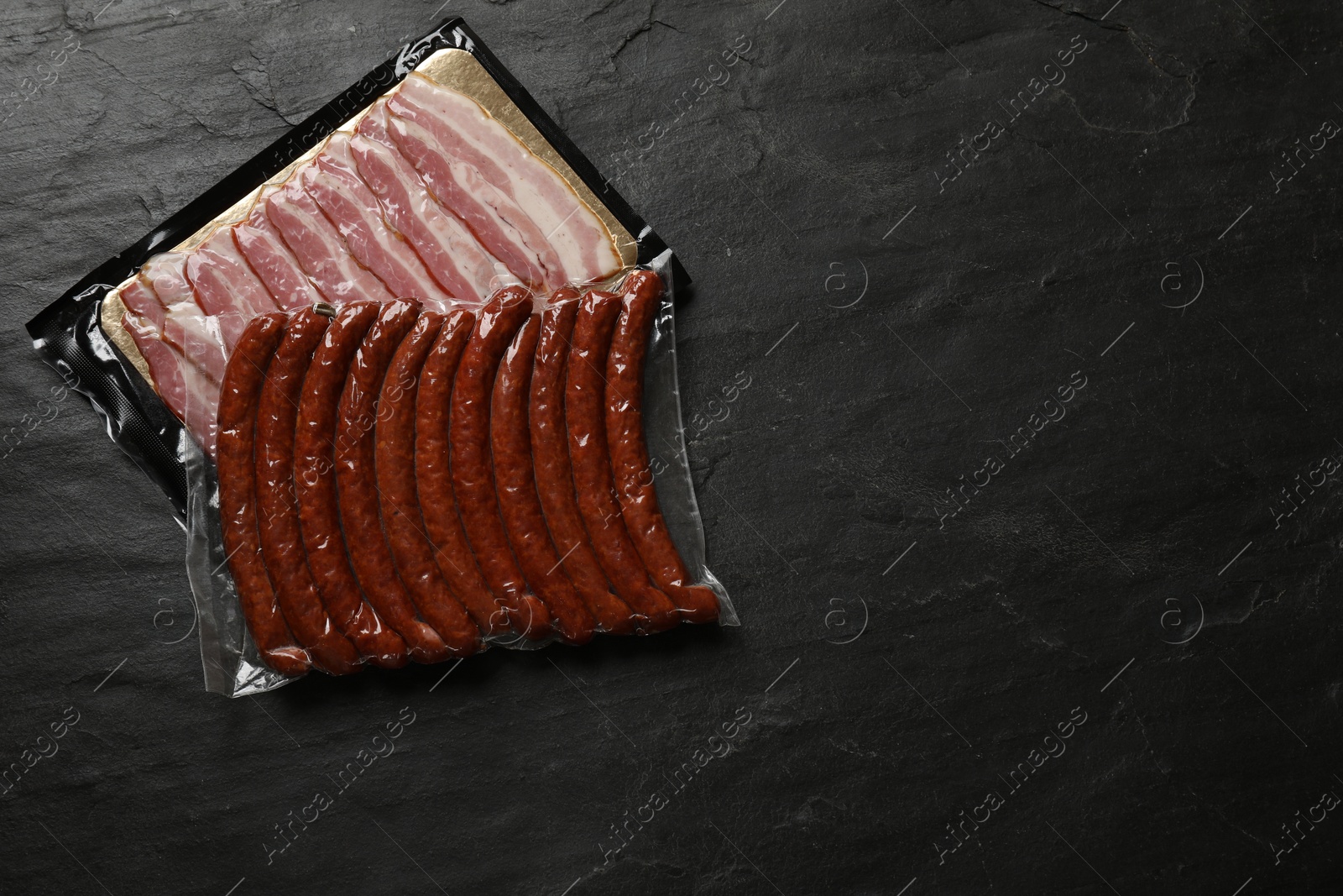 Photo of Packs of sausages and bacon on black table, top view. Space for text