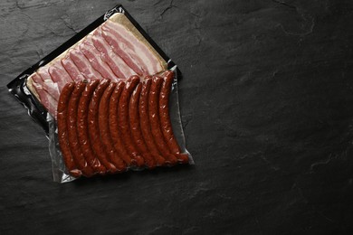 Packs of sausages and bacon on black table, top view. Space for text