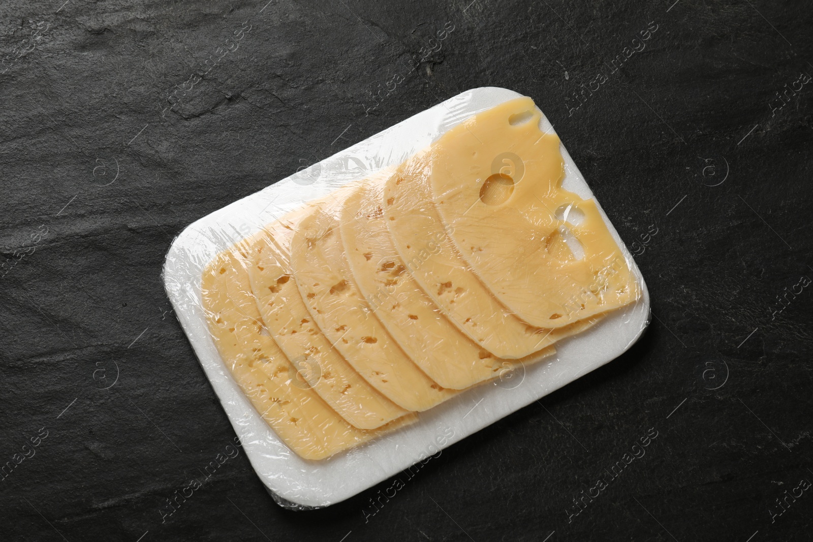 Photo of Pack of sliced cheese on black table, top view