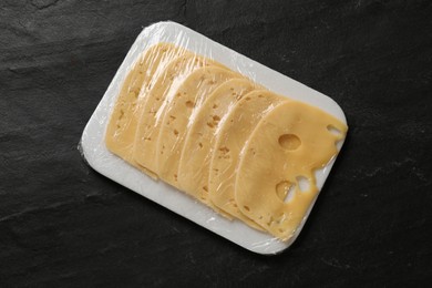 Photo of Pack of sliced cheese on black table, top view