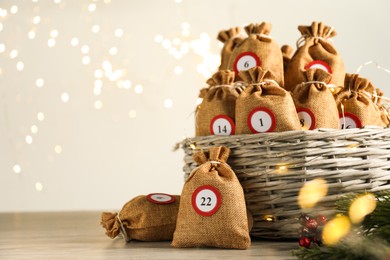 Photo of Advent calendar idea. Bags with numbers in basket on table against Christmas lights, space for text