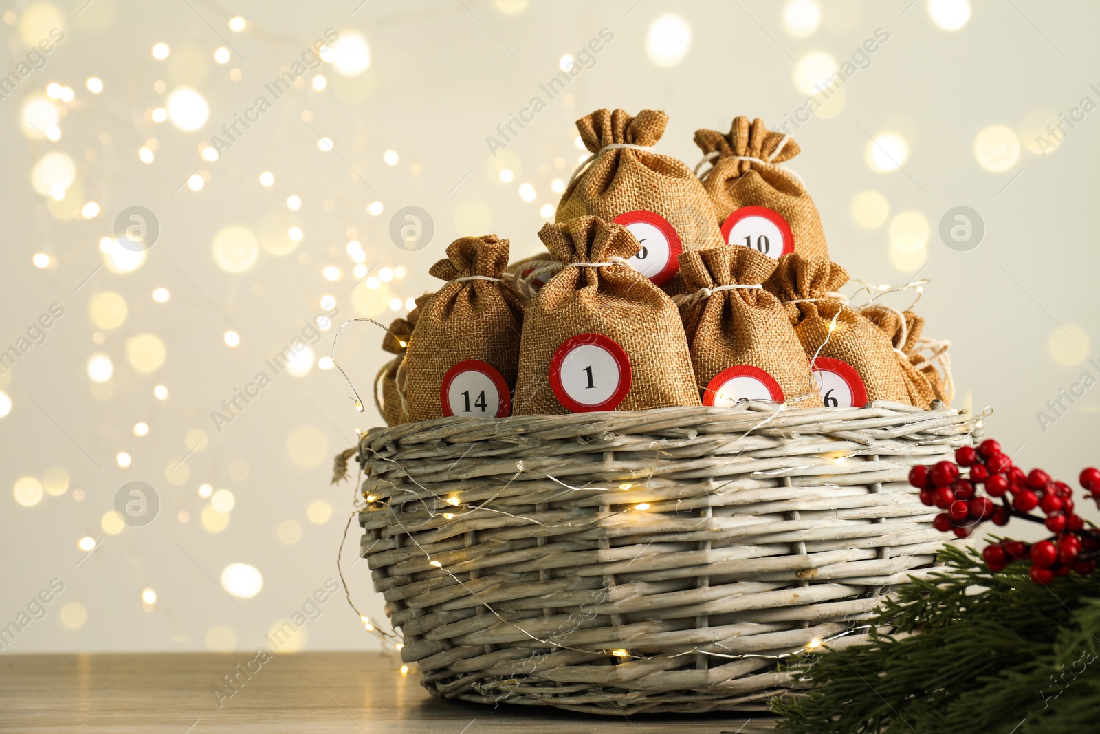 Photo of Advent calendar idea. Bags with numbers in basket on table against Christmas lights