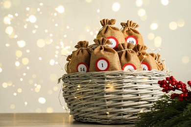 Photo of Advent calendar idea. Bags with numbers in basket on table against Christmas lights