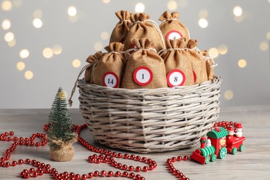 Photo of Advent calendar idea. Bags with numbers in basket and Christmas decor on table against blurred lights