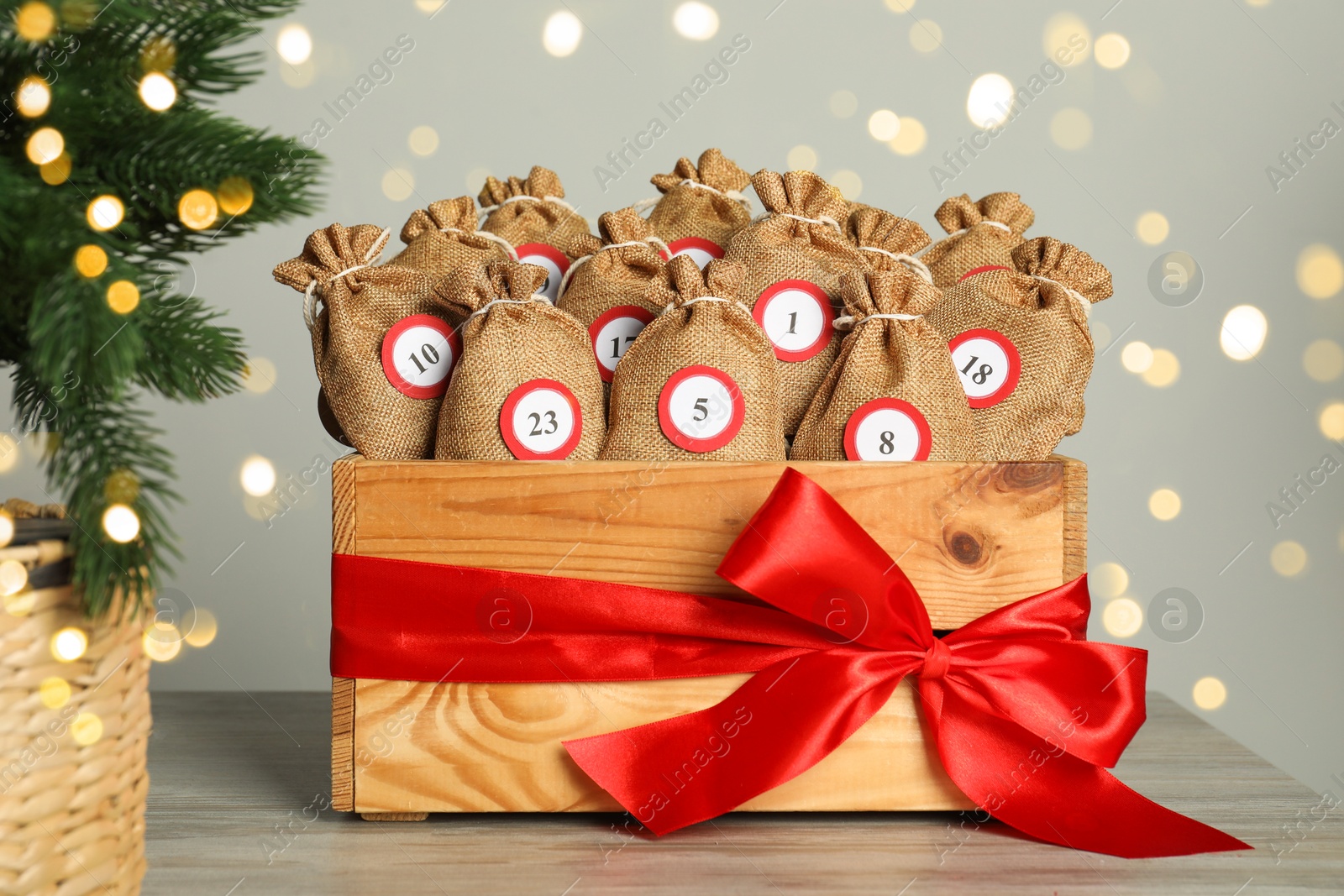 Photo of Advent calendar idea. Bags with numbers in wooden crate on table against Christmas lights