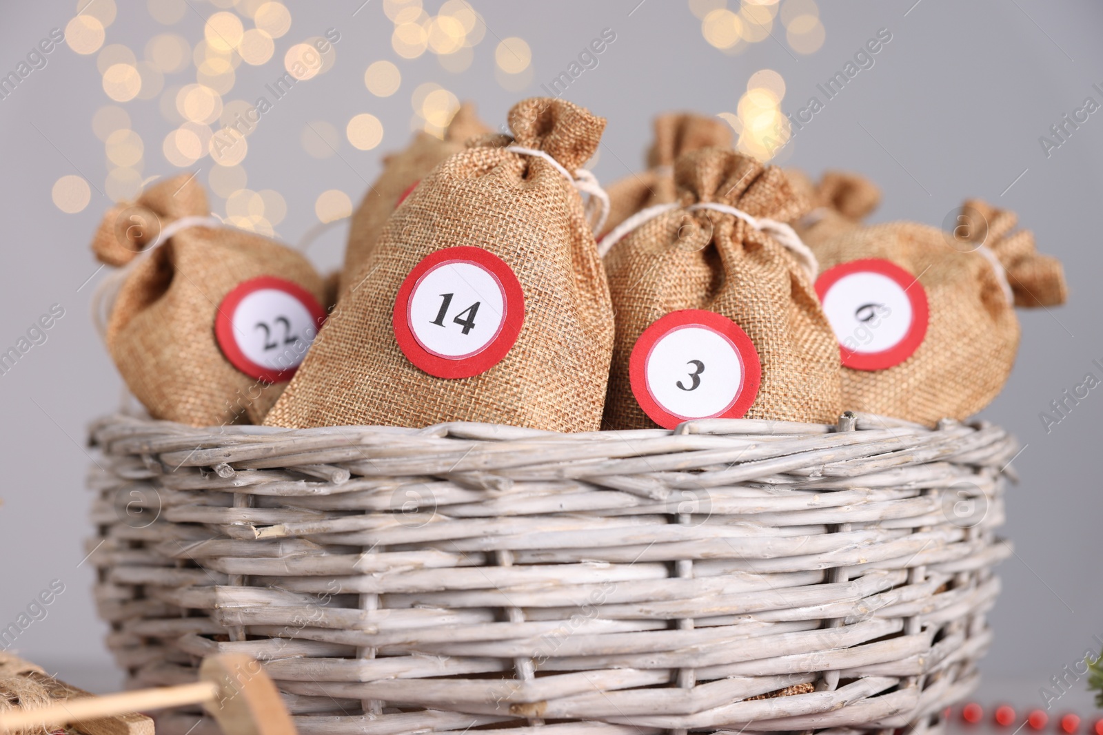 Photo of Christmas advent calendar with gifts in wicker basket on against blurred lights, closeup