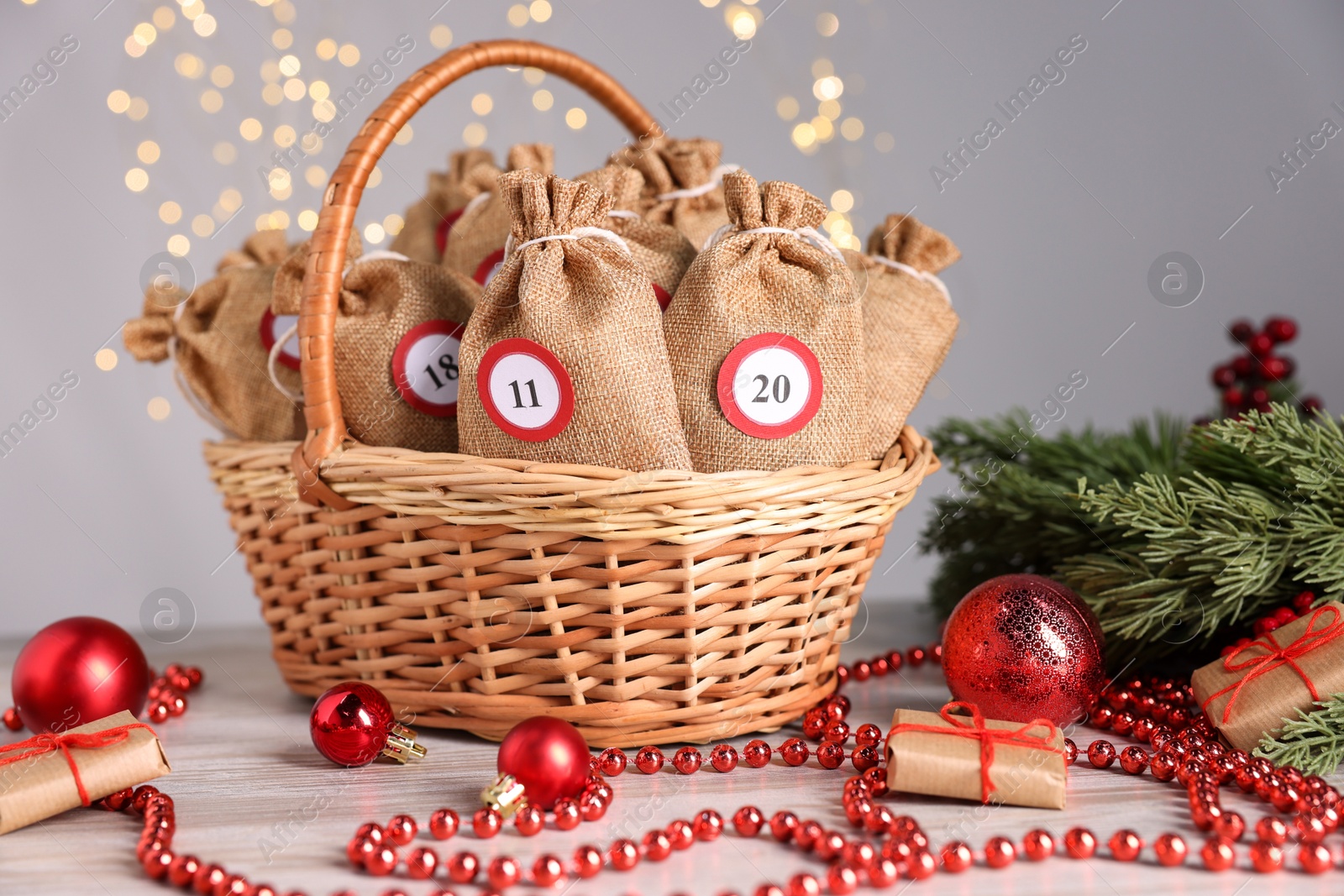 Photo of Christmas advent calendar with gifts in wicker basket and decor on wooden table against blurred lights