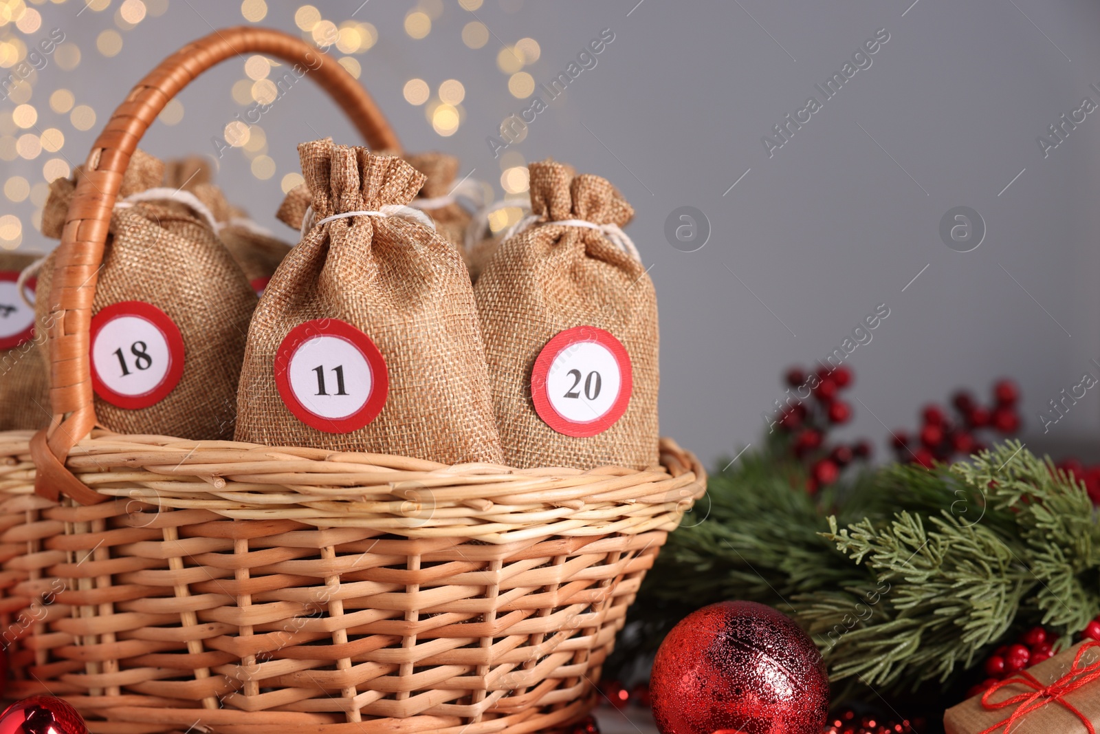 Photo of Christmas advent calendar with gifts in wicker basket and decor on table against blurred lights, closeup