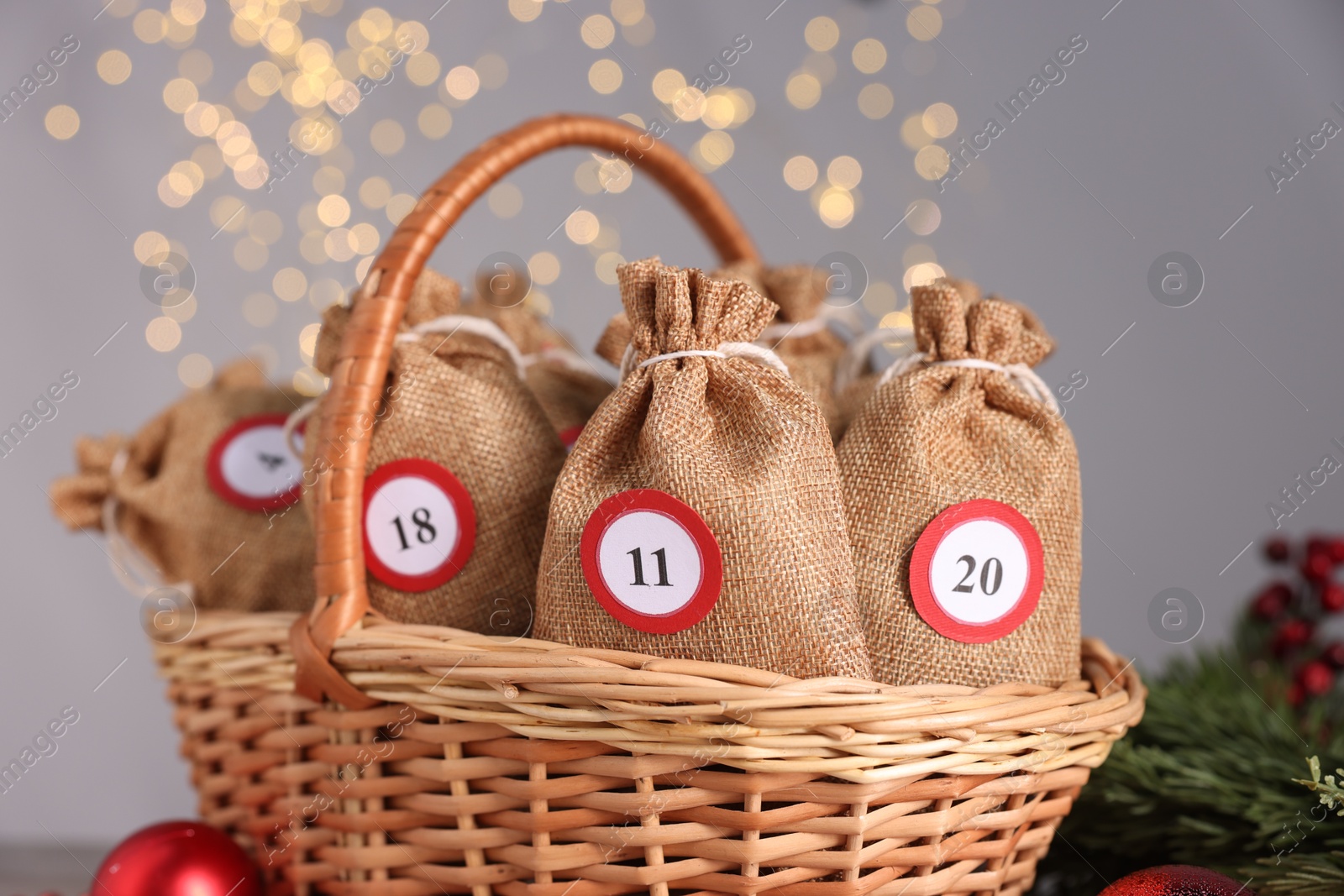 Photo of Christmas advent calendar with gifts in wicker basket and decor against blurred lights, closeup