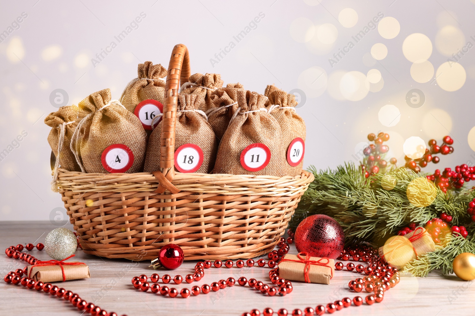 Photo of Christmas advent calendar with gifts in wicker basket and decor on wooden table against blurred lights