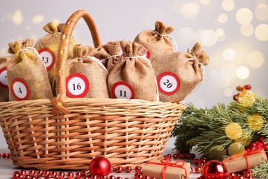 Photo of Christmas advent calendar with gifts in wicker basket and decor on table against blurred lights