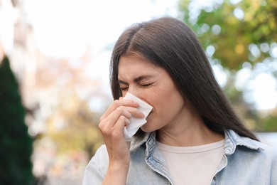 Woman with runny nose in park, space for text