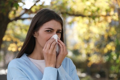 Woman with runny nose in park, space for text