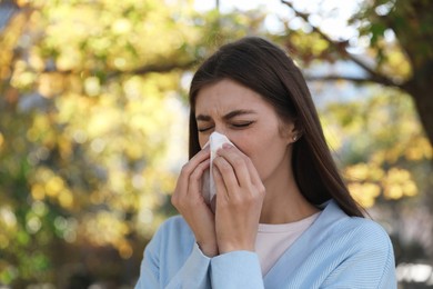 Woman with runny nose in park, space for text